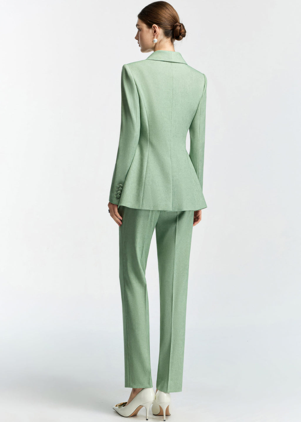 A rear view of the model, showcasing the back tailoring of the blazer, the flared hem of the jacket, and the fit of the slim trousers.