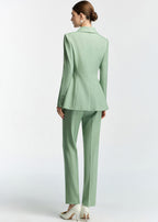 A rear view of the model, showcasing the back tailoring of the blazer, the flared hem of the jacket, and the fit of the slim trousers.