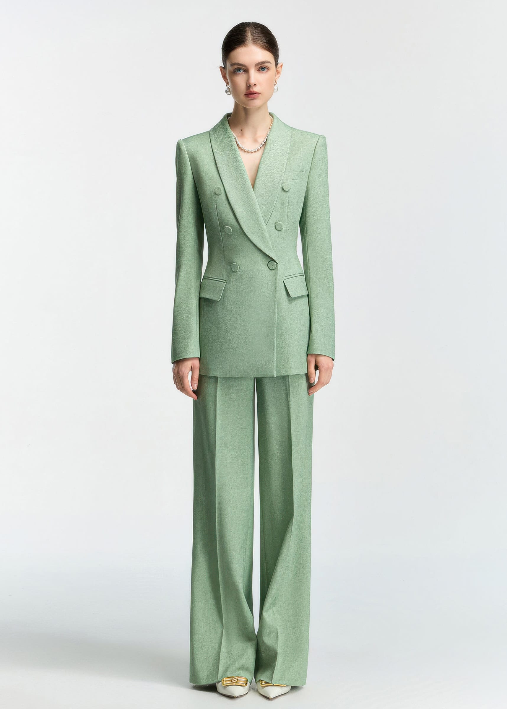 A front-facing full-length shot of a model wearing a mint green double-breasted blazer and matching wide-leg trousers.