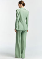 A rear view of the model, showing the tailoring, back seams, and fit of the mint green blazer and trousers.
