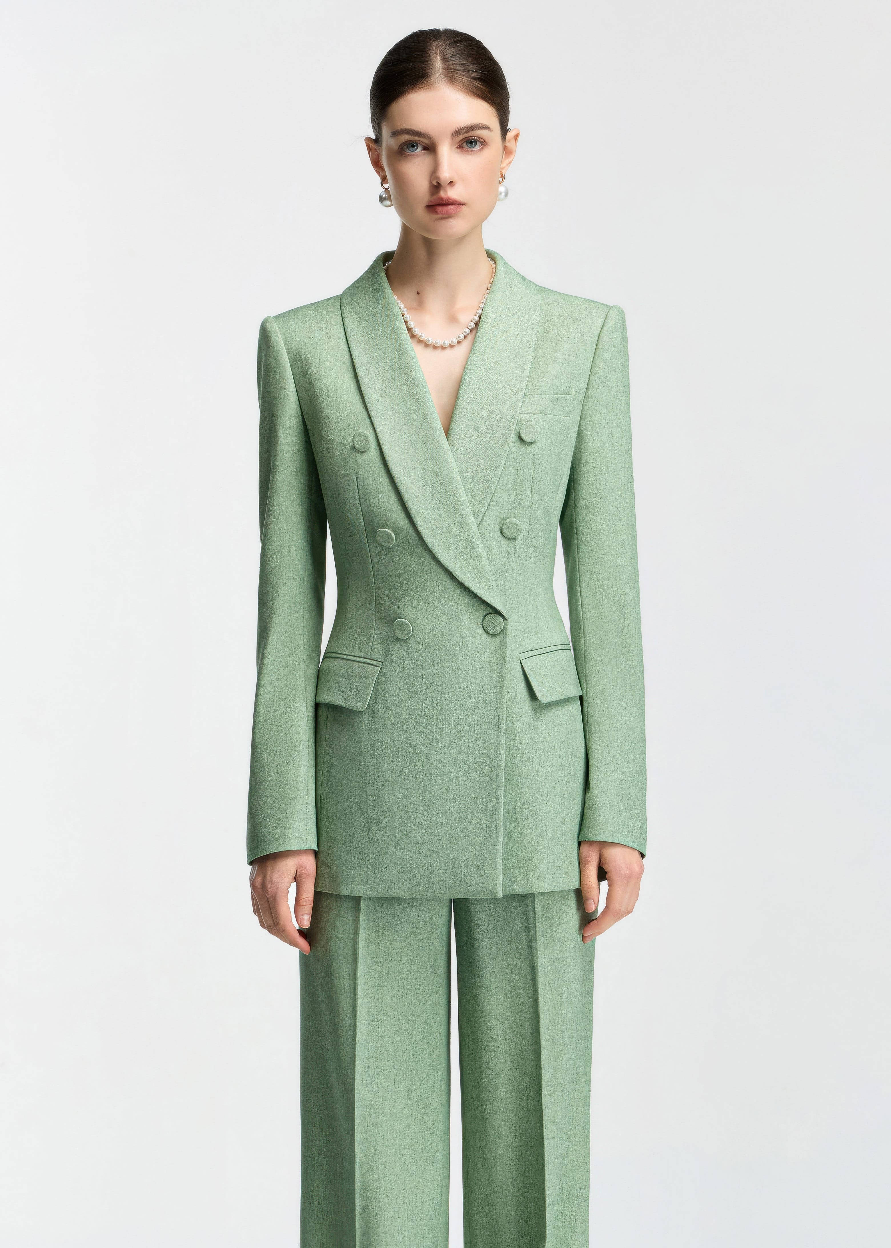 A straight-on studio portrait of the model in the mint green suit, focusing on the structured fit and pearl necklace accessory.