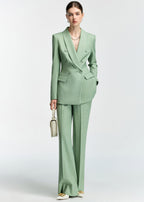 A full-length shot of the model standing and holding a small cream-colored handbag, paired with the mint green suit and white pointed-toe heels.