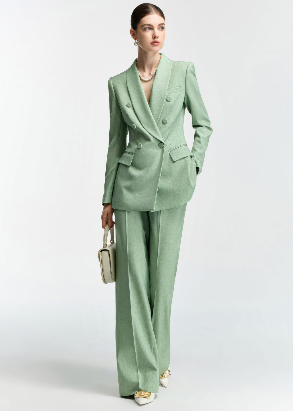 The model is captured mid-stride or posing with a handbag, showing the movement of the mint green suit fabric.