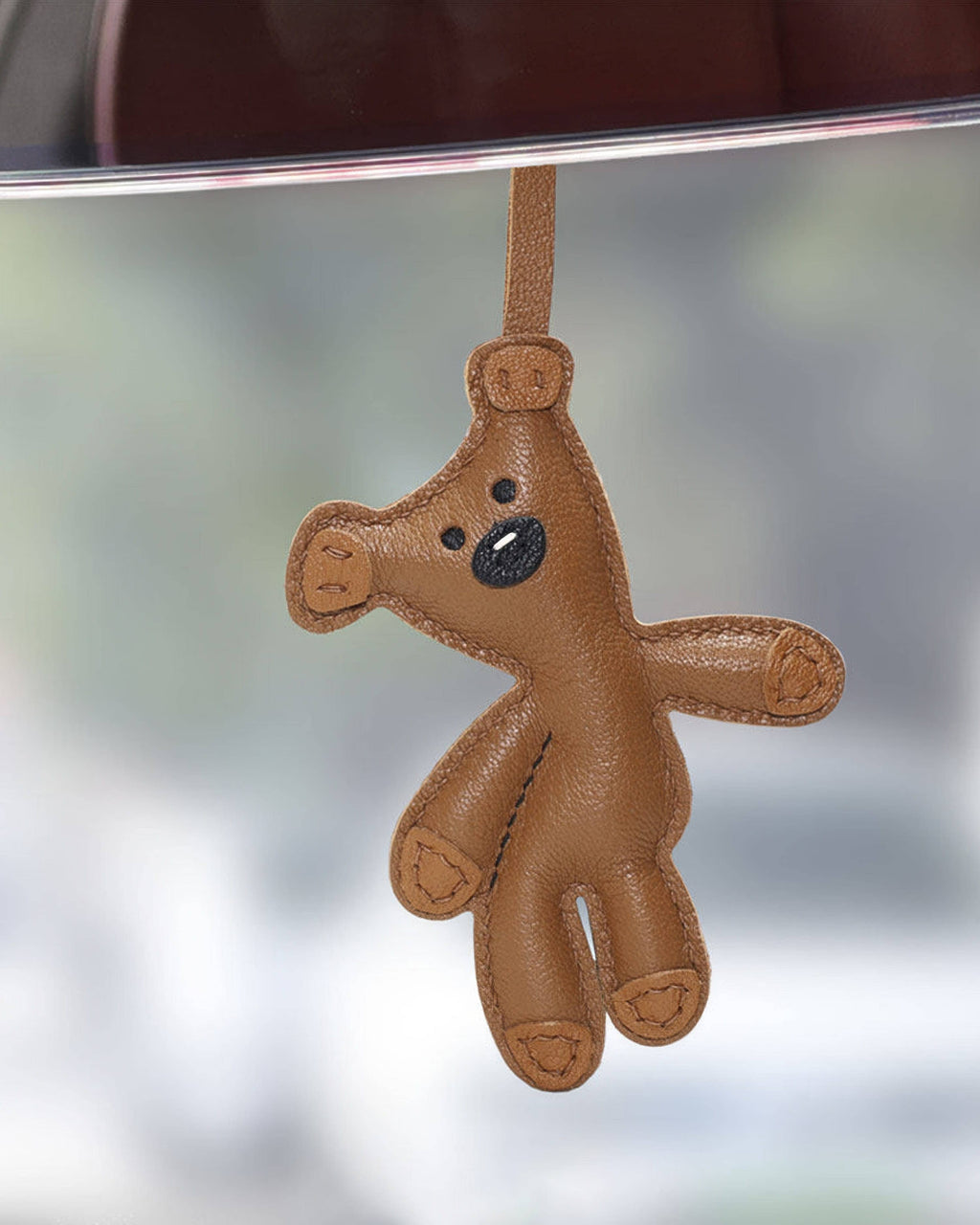 Handcrafted brown leather teddy bear bag charm hanging as a decorative car rear view mirror accessory.
