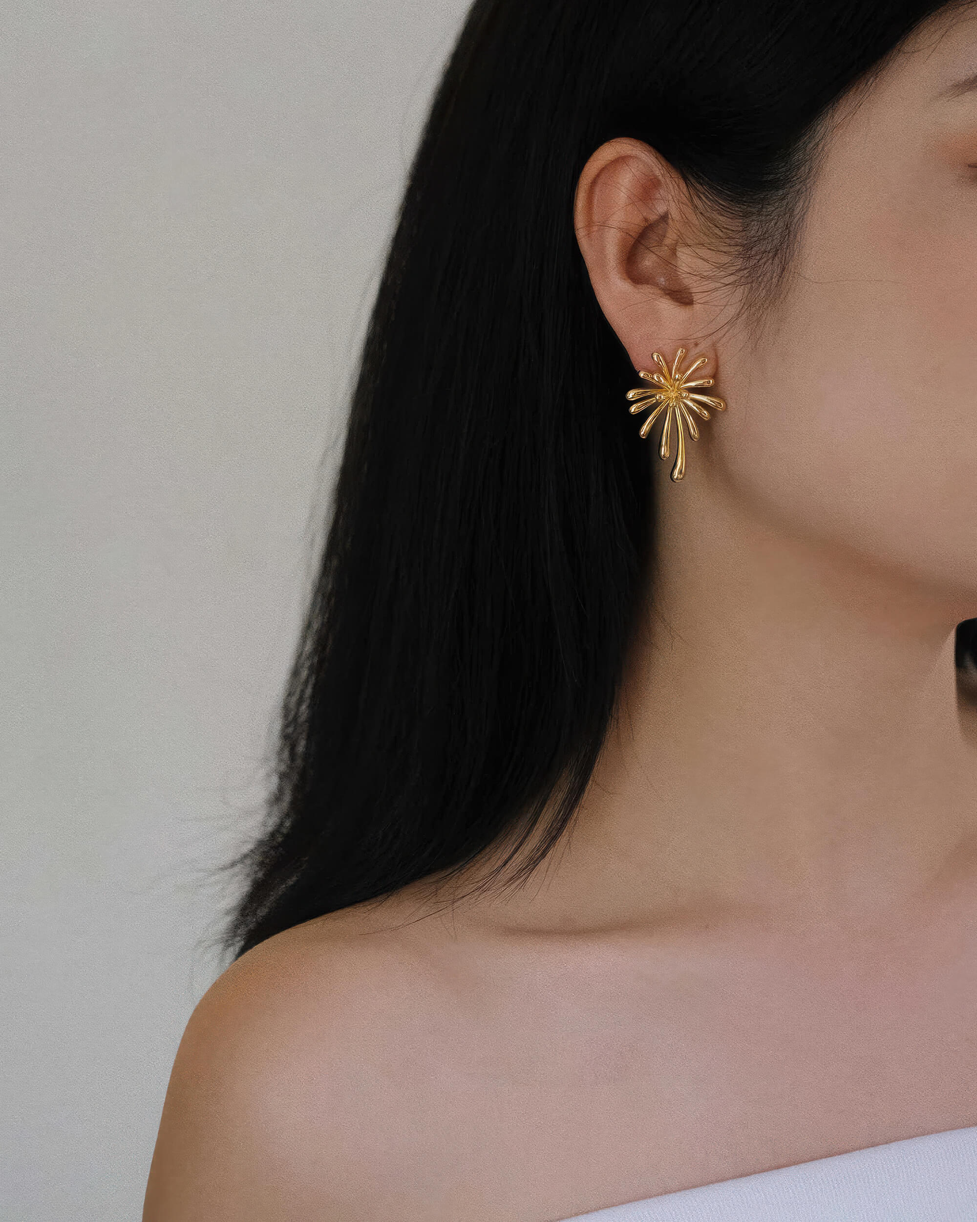 Side view of a model wearing a Radiant 18K gold plated burst stud earring with a minimalist white outfit.