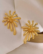 Pair of 18K gold plated burst stud earrings displayed on a soft cream fabric background, highlighting the luxury aesthetic.