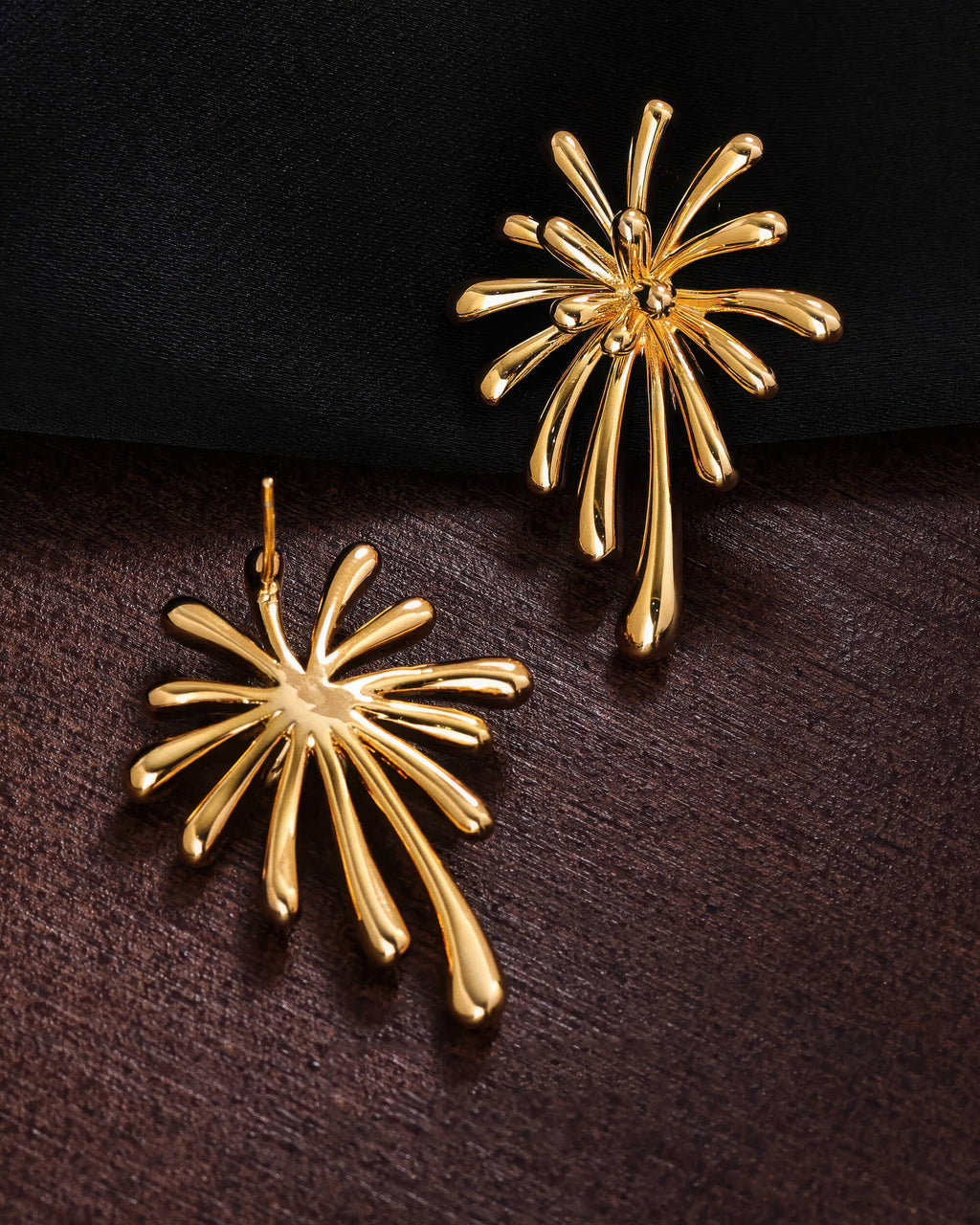 Front and back view of the 18K gold plated burst earrings on a dark textured surface, showing the secure stud post.