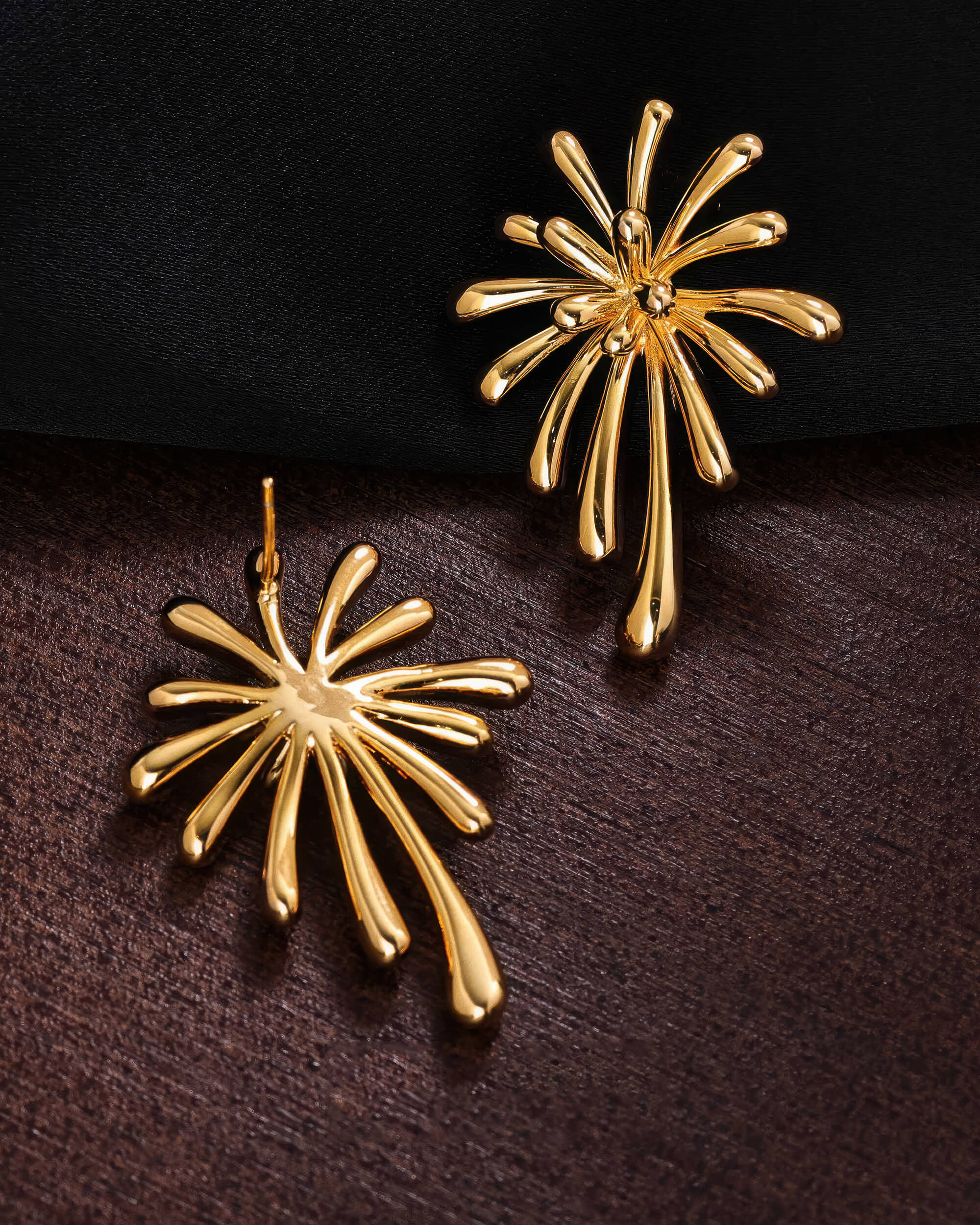 Front and back view of the 18K gold plated burst earrings on a dark textured surface, showing the secure stud post.