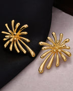 High-angle shot of the sunburst-shaped gold earrings on a contrasting black and grey background.