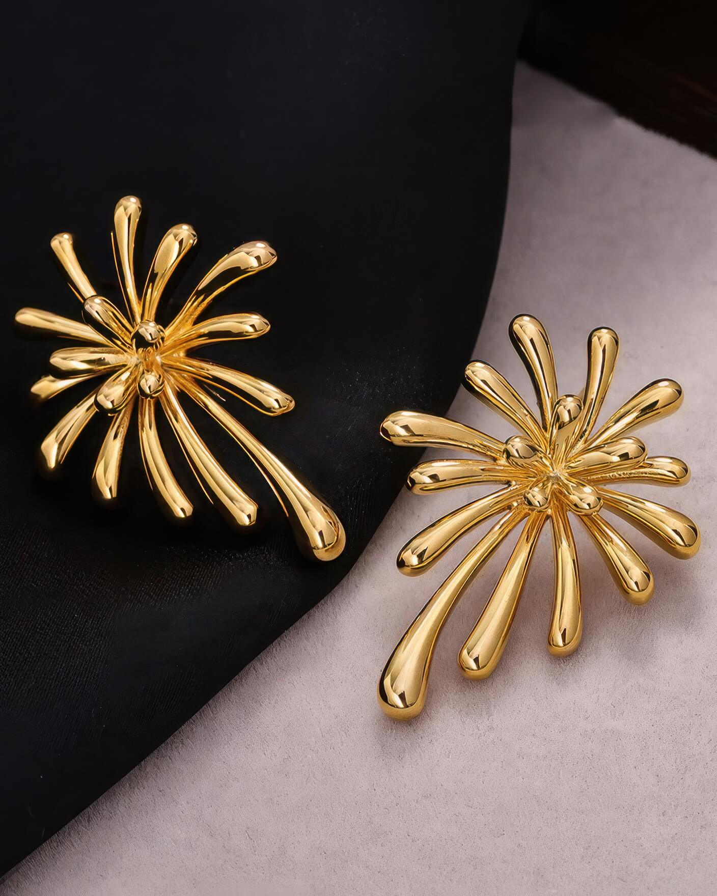 High-angle shot of the sunburst-shaped gold earrings on a contrasting black and grey background.
