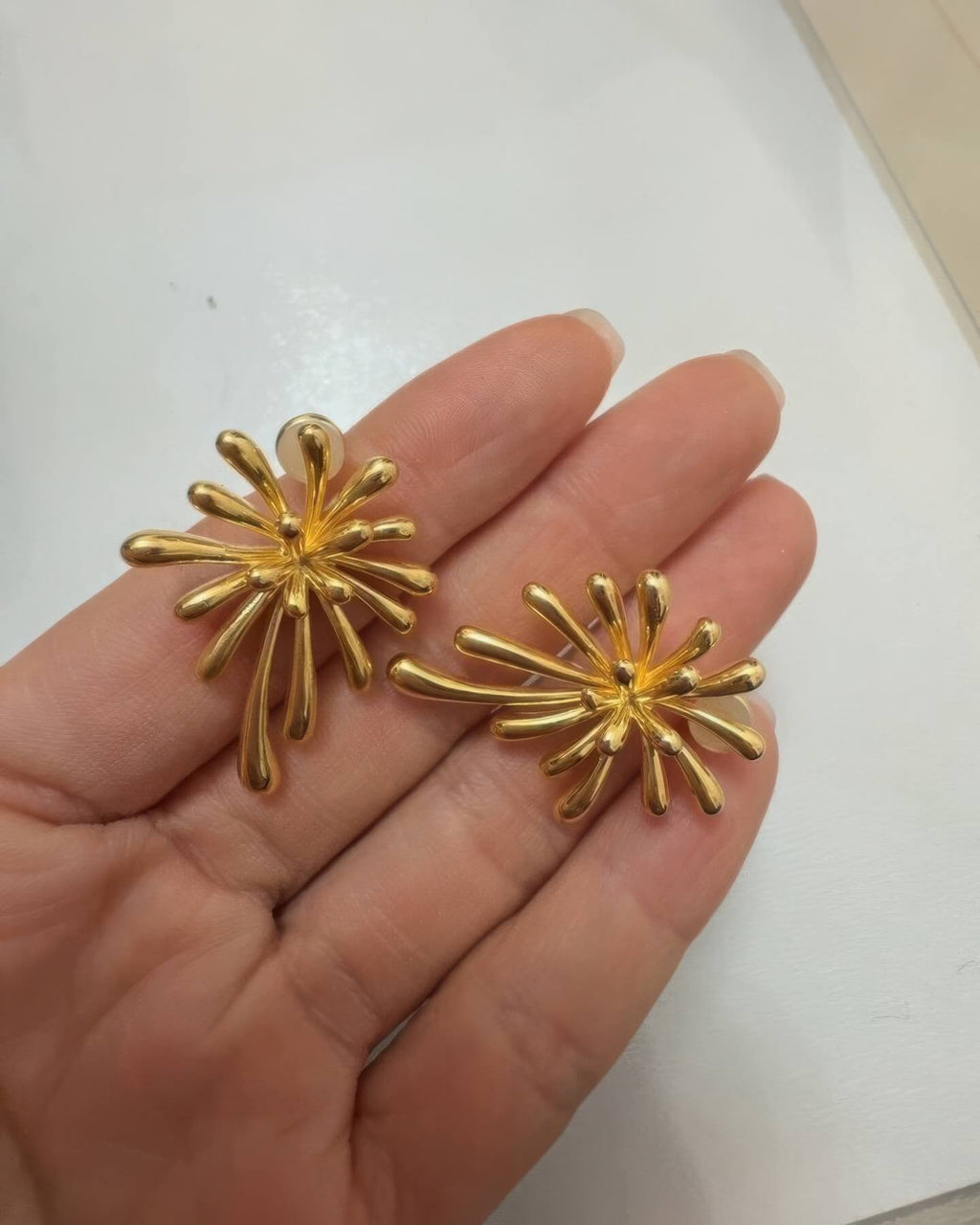Hand-held photo of the 18K gold plated burst earrings to show real-life scale and lightweight design.