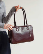 A woman holding the long straps of a burgundy distressed leather Boston bag with a silver key charm.
