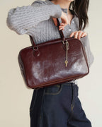 Professional shot of a burgundy distressed leather Boston bag with dual top handles.