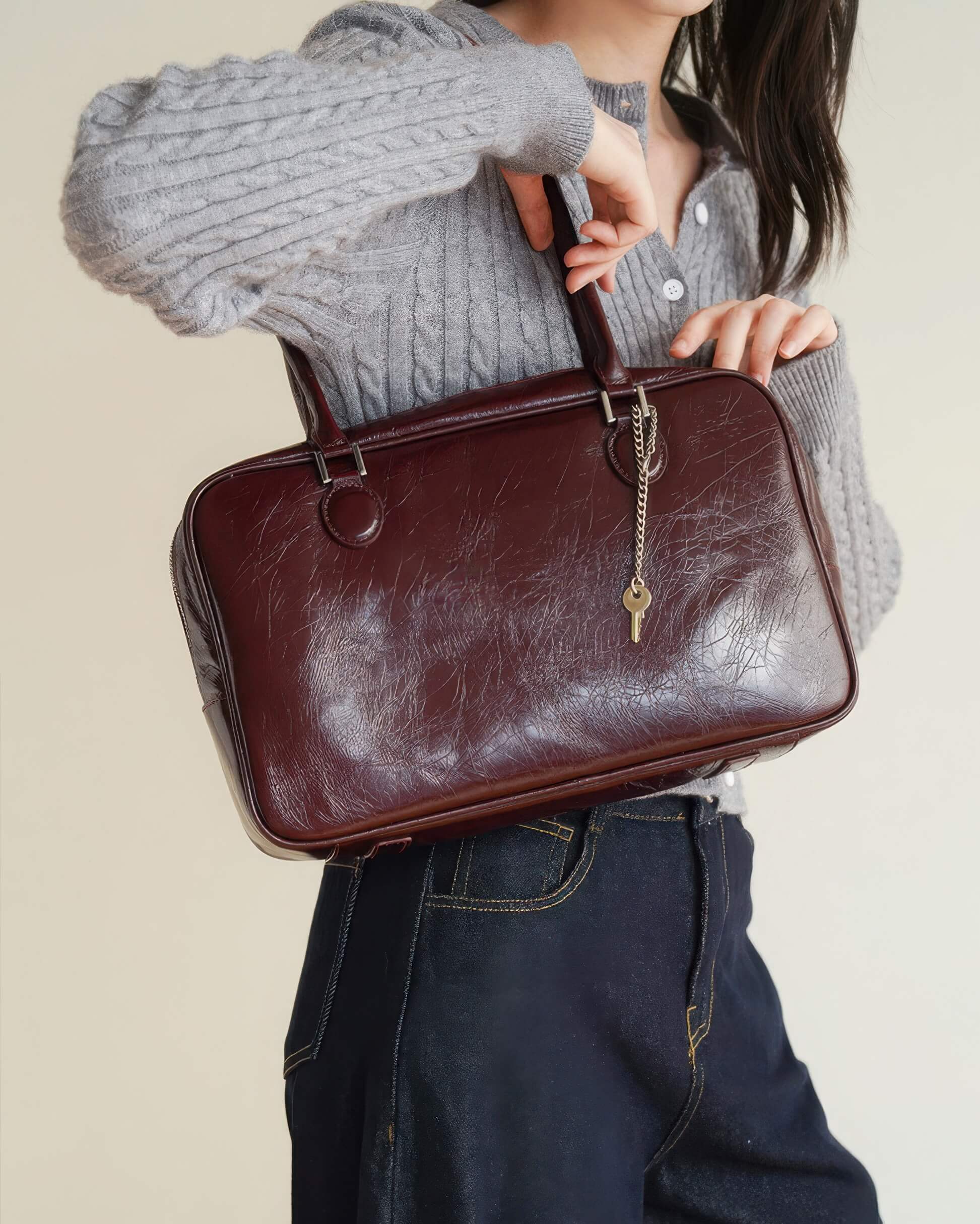 Professional shot of a burgundy distressed leather Boston bag with dual top handles.