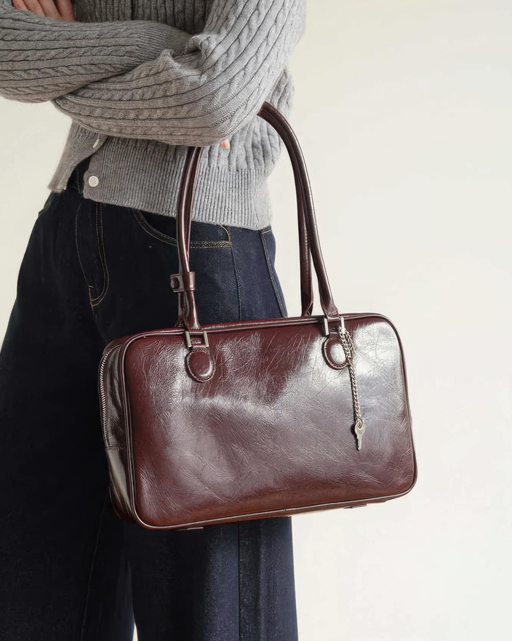 Model holding a dark cherry distressed leather shoulder bag with silver key charm.