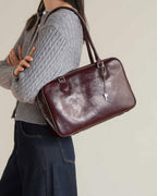 Side view of woman wearing a grey cable knit cardigan and mahogany leather handbag.