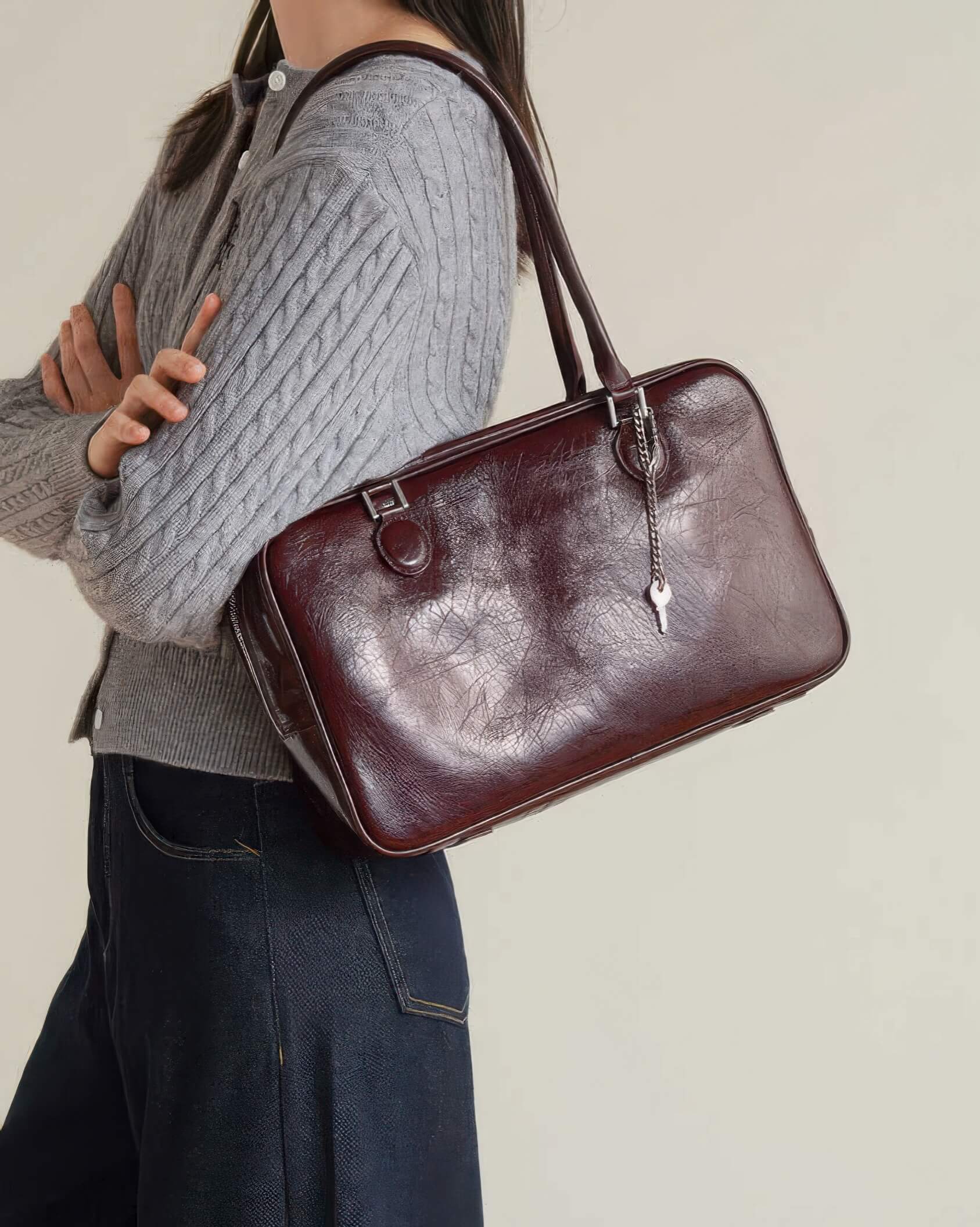 Side view of woman wearing a grey cable knit cardigan and mahogany leather handbag.