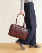 Full body shot of model carrying a classic burgundy briefcase-style leather bag.