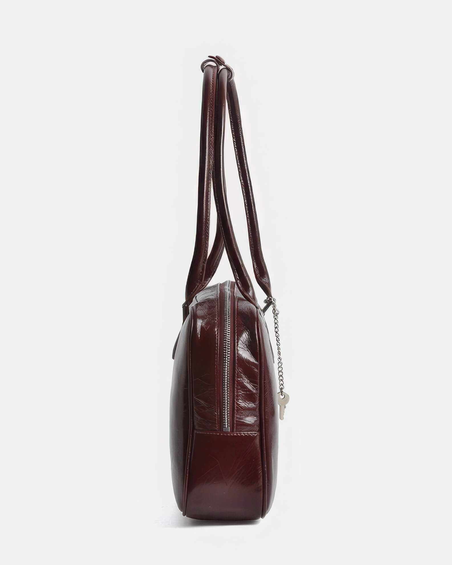 Side profile of a slim burgundy leather satchel showing zipper detail and strap length.