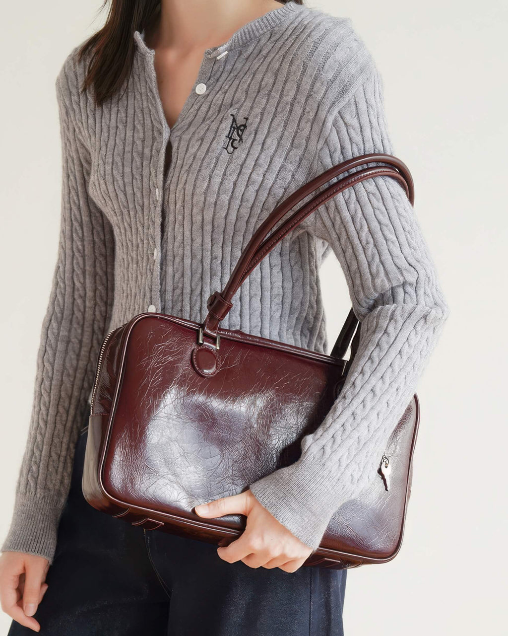 Woman carrying a retro-style burgundy leather handbag under arm, lifestyle shot.