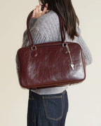 Back view of model wearing a grey sweater with a large mahogany leather shoulder bag.