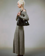 Full-body view of blonde model in a long grey dress holding a black star studded slouchy shoulder bag