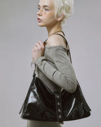 Close-up side profile of model wearing black glossy slouchy handbag featuring silver star studs on the center strap