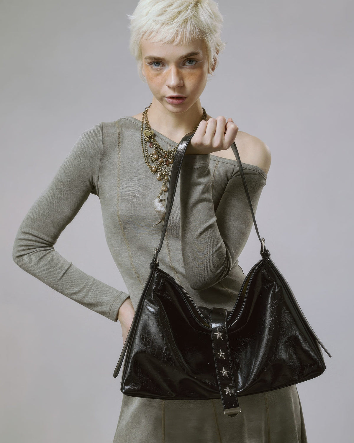 Front view pose of model holding a black soft faux leather slouchy purse with star rivet details