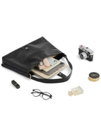 Flat lay shot of black faux leather shoulder bag next to camera, glasses, tablet, and cosmetics on white background