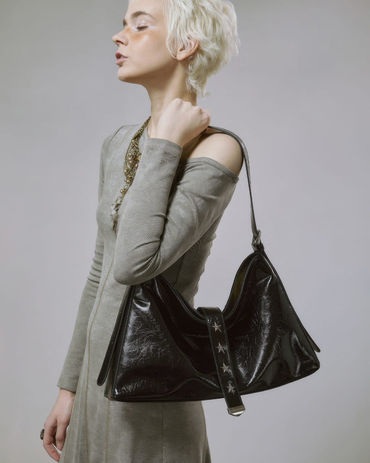 Side view of model looking up while carrying a slouchy black shiny leather handbag over her shoulder