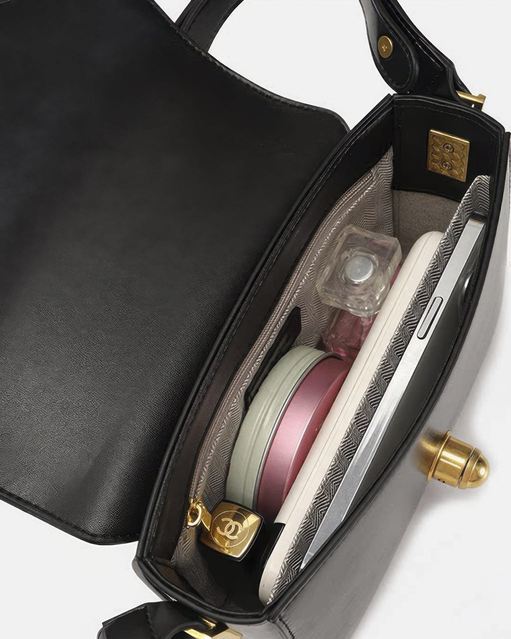 Interior view of black leather flap crossbody bag filled with daily essentials including makeup compact, perfume, lipstick, and smartphone.