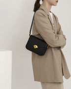 Model in a beige oversized suit carrying a black leather flap crossbody bag over her shoulder.