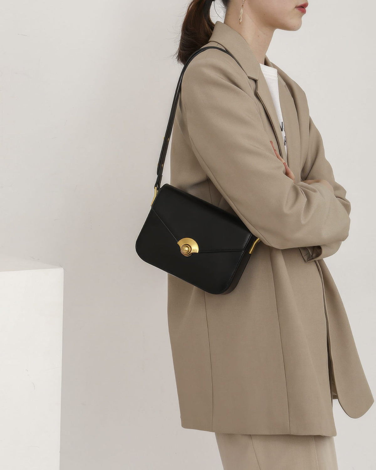 Model in a beige oversized suit carrying a black leather flap crossbody bag over her shoulder.