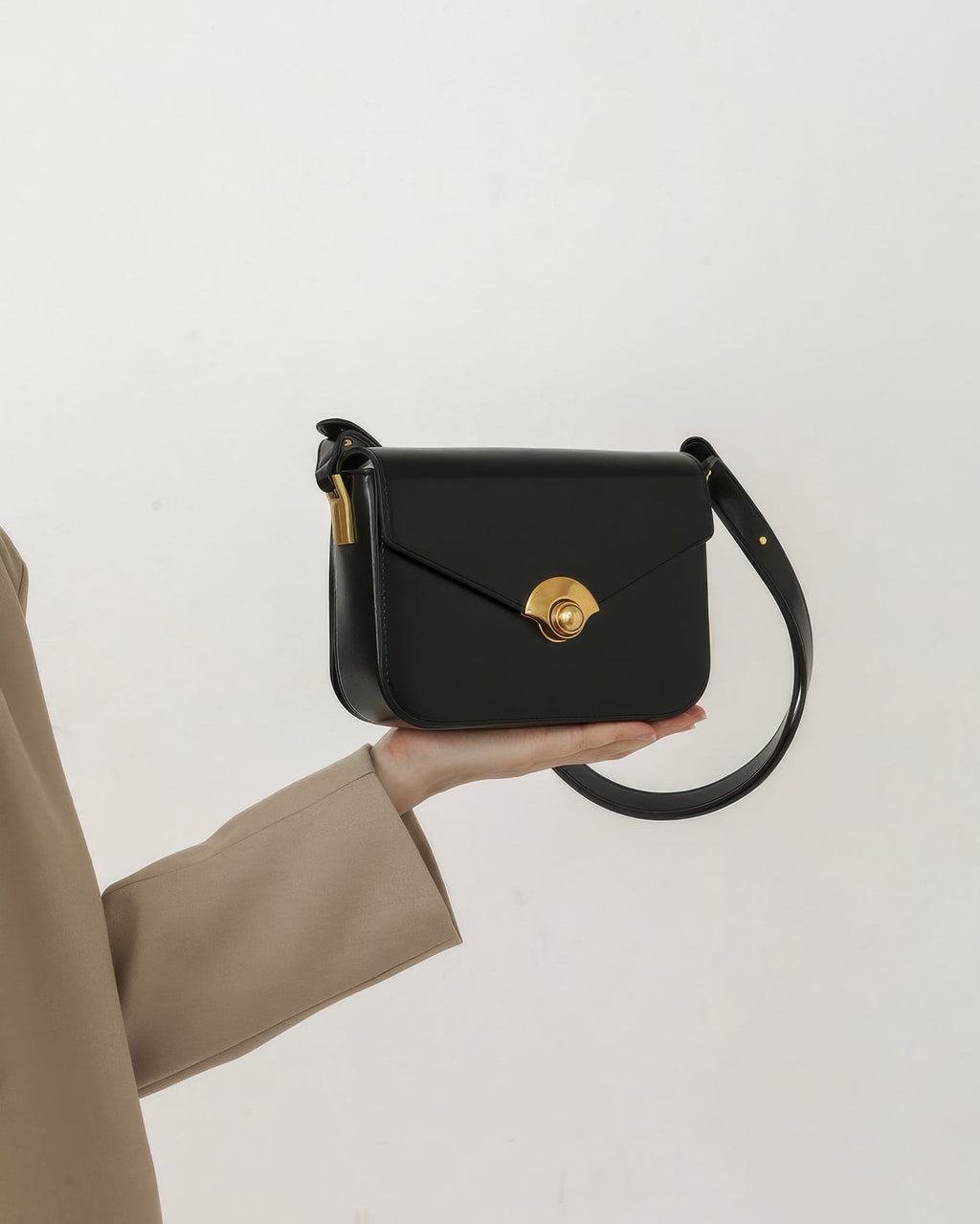 Model holding a black leather flap handbag with a fan-shaped gold turn-lock closure in hand.
