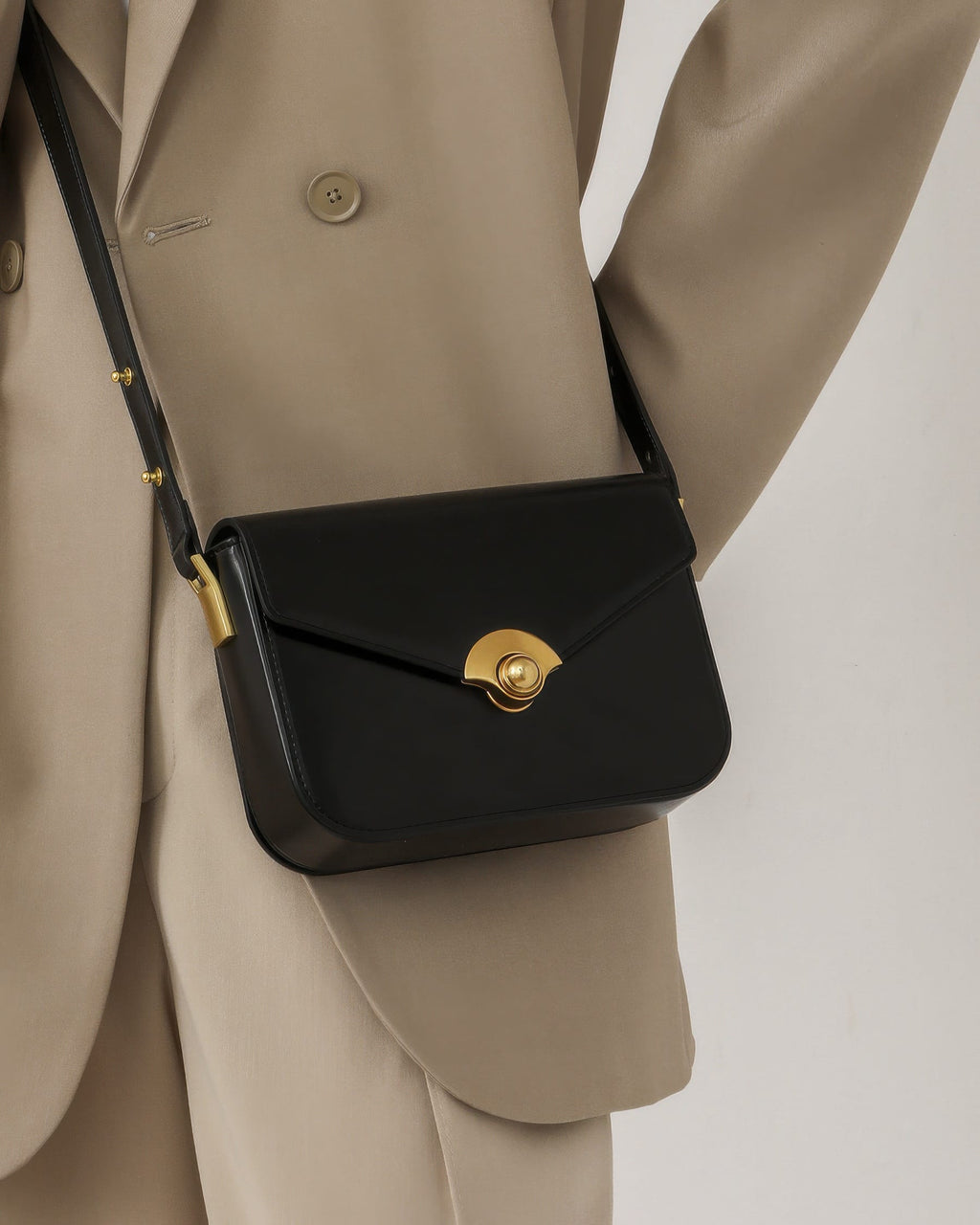 Close-up of a model wearing a black leather turn-lock flap bag across a tailored beige blazer.