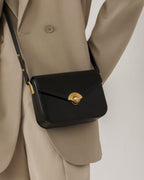 Close-up of a model wearing a black leather turn-lock flap bag across a tailored beige blazer.