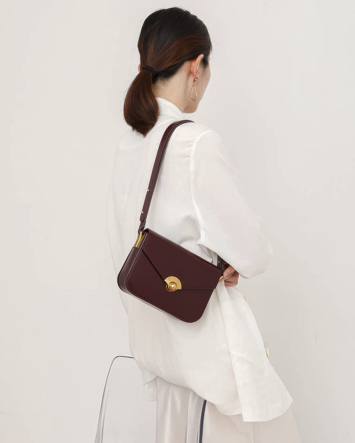 Woman in white outfit wearing a dark brown leather turn-lock flap shoulder bag.