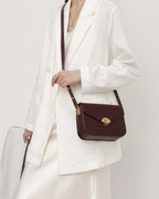 Model styling a deep brown leather flap crossbody purse with gold turn-lock closure and white blazer.