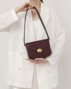 Woman holding a dark burgundy leather flap shoulder bag with gold hardware clasp.