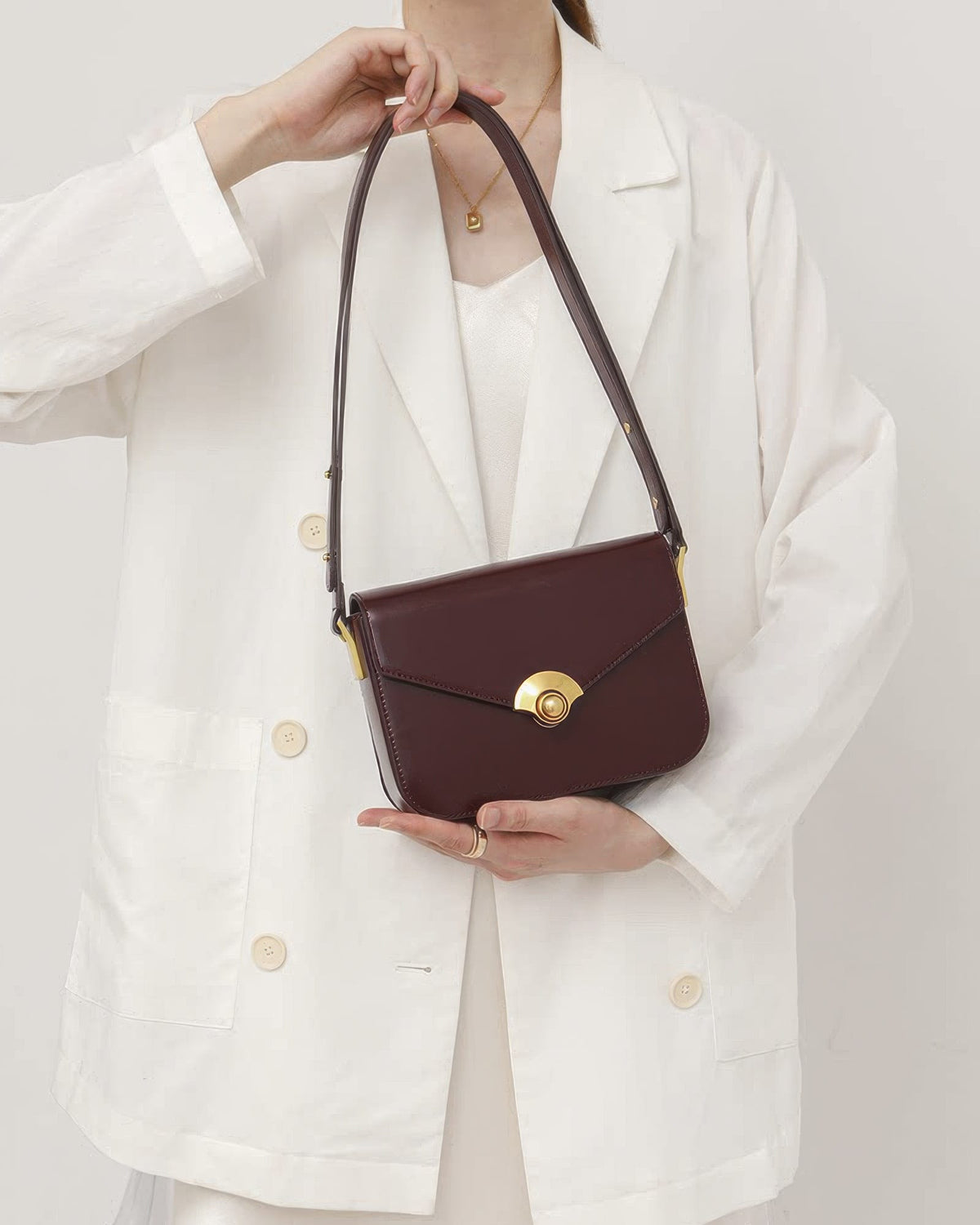 Woman holding a dark burgundy leather flap shoulder bag with gold hardware clasp.