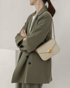 Model in an olive green suit wearing an off-white leather flap shoulder bag.
