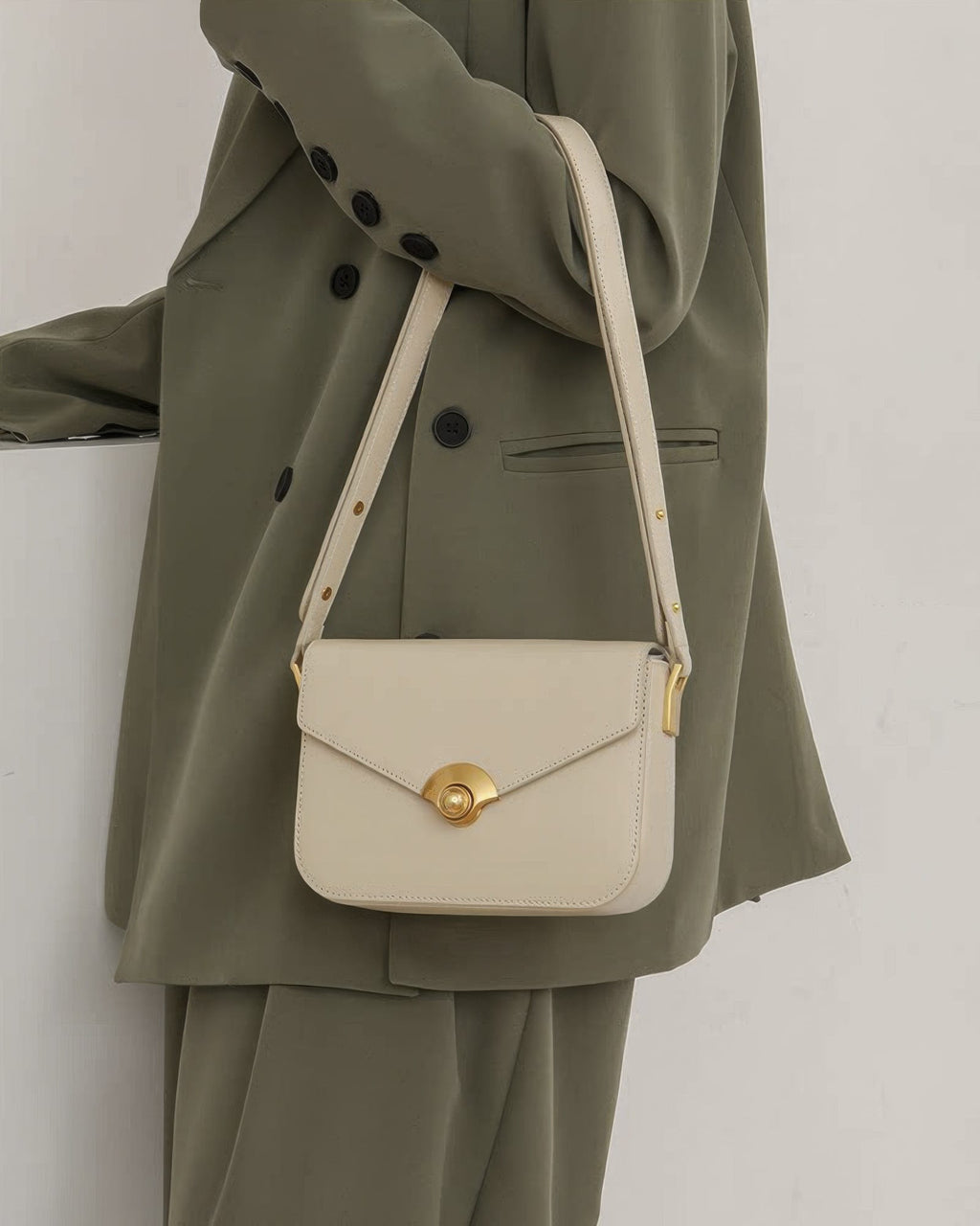 Close-up of model wearing an off-white leather crossbody bag with a gold turn-lock closure.