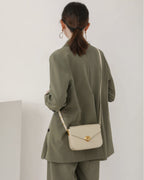 Back side view of a model in an olive green blazer outfit wearing an off-white leather flap crossbody bag.