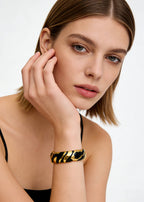Model wearing the black and gold Vintage Zebra Stripe Enamel Cuff Bracelet on her wrist while resting her chin on her hand.