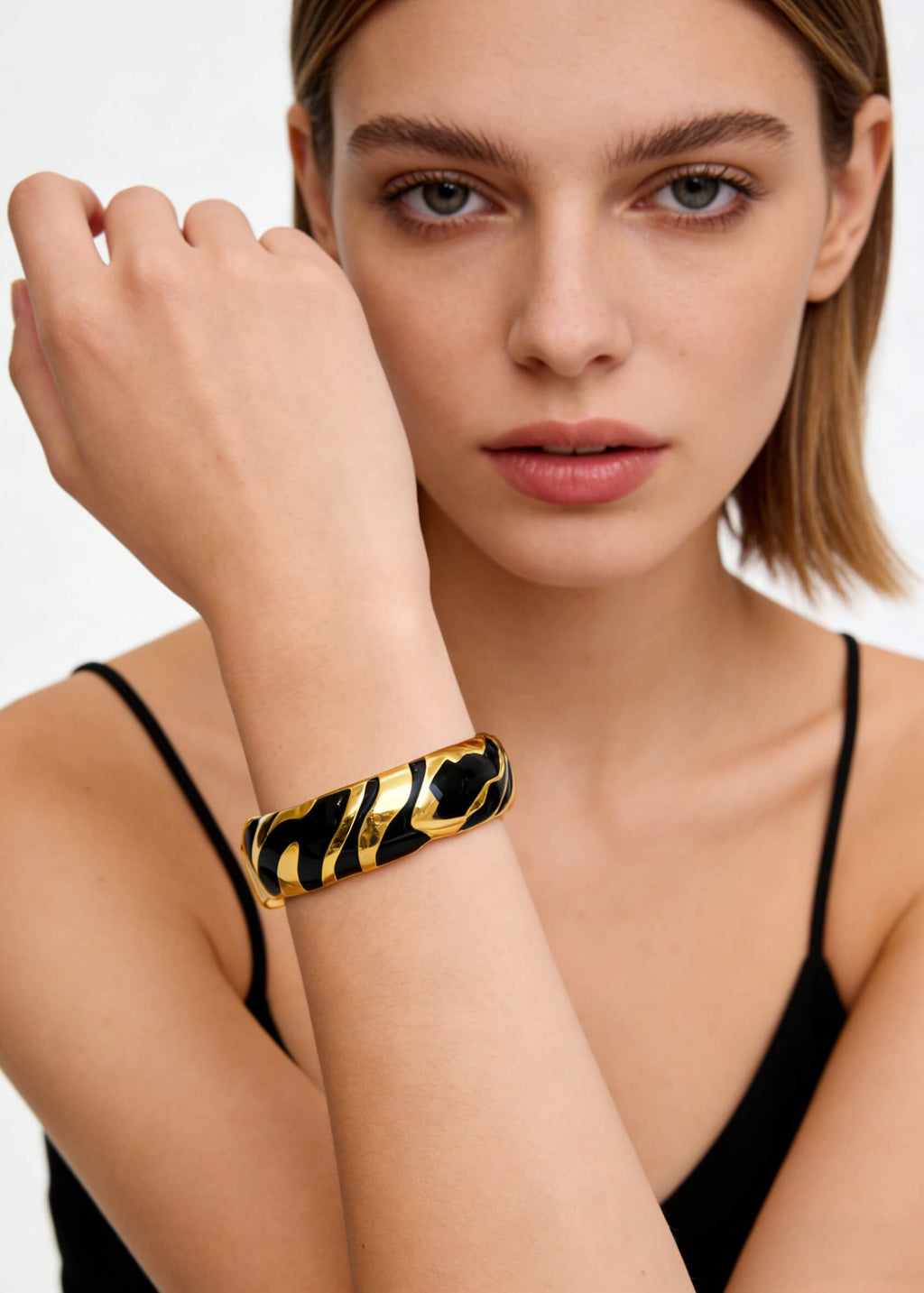 Close-up of the Vintage Zebra Stripe Enamel Cuff Bracelet in black and gold styled with a black tank top.
