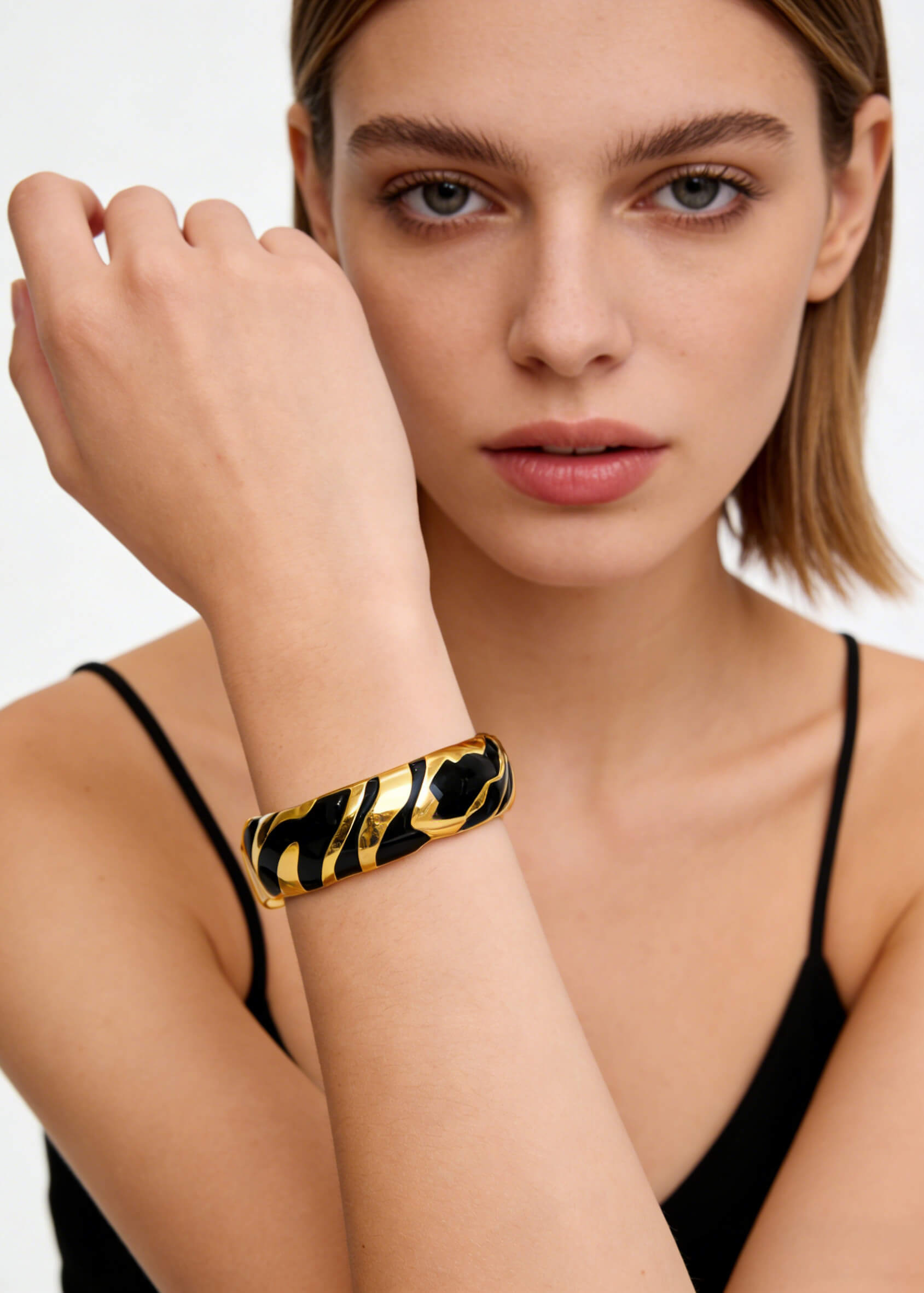 Close-up of the Vintage Zebra Stripe Enamel Cuff Bracelet in black and gold styled with a black tank top.