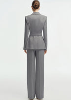 Rear view of a woman wearing a tailored grey business suit featuring a belted waist and wide-leg trousers.