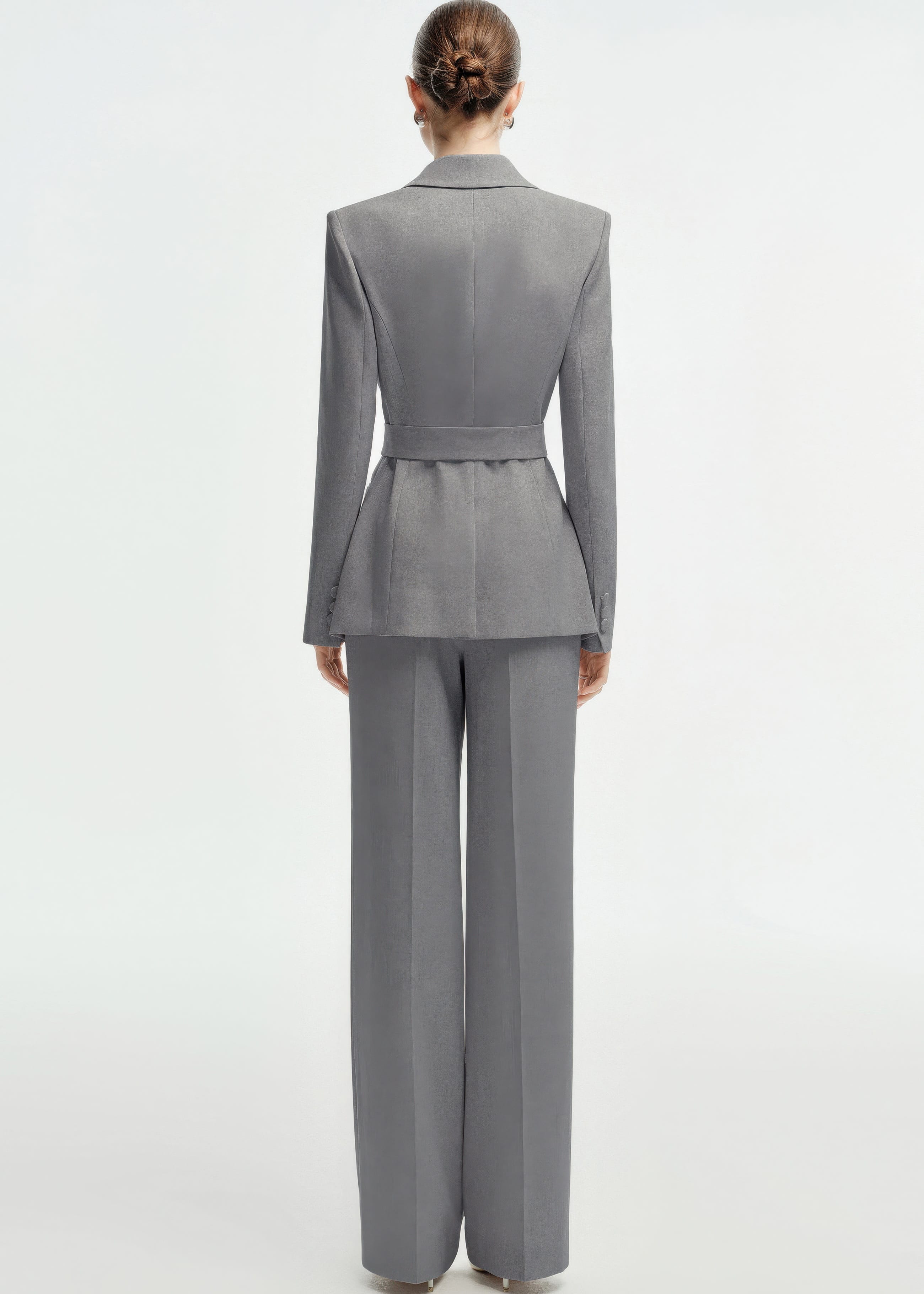 Rear view of a woman wearing a tailored grey business suit featuring a belted waist and wide-leg trousers.