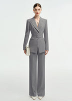 Full-length front view of a woman posing in a professional grey belted suit with white pointed-toe heels.