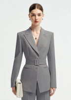 Close-up portrait of a woman wearing a grey belted suit jacket with sharp lapels and a silver pendant necklace.
